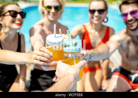 Les amis de trinquer avec bouteilles de boissons d'été sur la piscine en plein air, close-up Banque D'Images