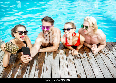Un groupe d'amis heureux photo selfies avec téléphone, tout en s'amusant sur la piscine en plein air pendant l'été Banque D'Images