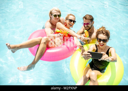 Jeune et heureux les amis faire inlatable selfies photo avec joints toriques et pistolets à eau dans la piscine, profiter de l'été en plein air Banque D'Images