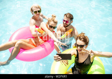 Jeune et heureux les amis faire inlatable selfies photo avec joints toriques et pistolets à eau dans la piscine, profiter de l'été en plein air Banque D'Images