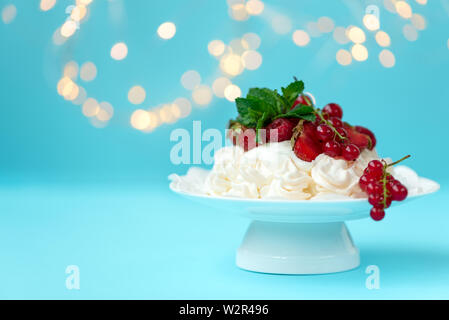 Pavlova anniversaire gâteau de fruit avec fraise, framboise, groseille rouge et de feuilles de menthe sur fond bleu pastel contre Lumières floues. Focus sélectif. Banque D'Images