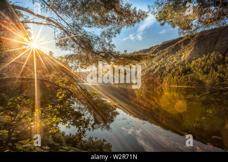 Glendalough, co. Wicklow / Irlande les rayons du soleil du matin éclairent la rive nord du lac supérieur dans la vallée de Glendalough Banque D'Images