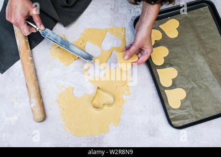 High angle portrait de personne à l'aide de couteau pour déplacer les cookies en forme de cœur sur une plaque à pâtisserie. Banque D'Images