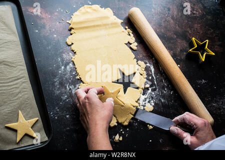 High angle portrait de personne coupure du levage des cookies en forme d'étoiles sur une plaque de cuisson avec un couteau. Banque D'Images