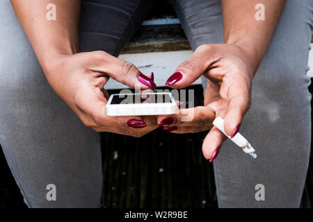 Une femme, main tenant une cigarette et des sms sur son téléphone intelligent. Banque D'Images