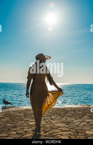 Jolie jeune femme en robe jaune à pied par stone beach Banque D'Images