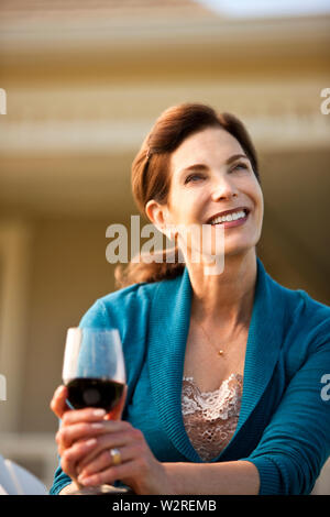 Femme mature jouit de verre de vin rouge dans sa cour arrière. Banque D'Images