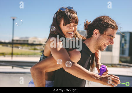 Couple à l'extérieur. Man piggybacking woman Playing with bulle de savon à l'extérieur. Banque D'Images