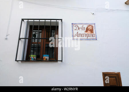 Chambre avec fenêtre barres en fer forgé dans le village de Frigiliana, Espagne avec nom de rue en tuile et image du Christ : Calle de la Amargura. Banque D'Images