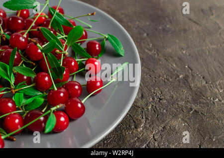 ,Lumineux, rouge cerise mûre berry dans une soucoupe gris béton, sur un vieux fond rustique. Banque D'Images