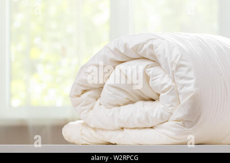 Une couette pliée rouleaux est couchée sur la commode dans le contexte d'une vitre brouillée. Ménage. Banque D'Images