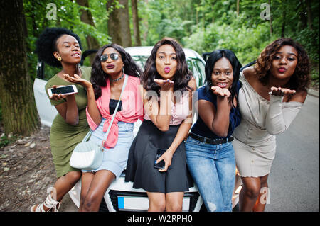 Groupe de cinq happy african american girls assis sur un capot de voiture. Banque D'Images