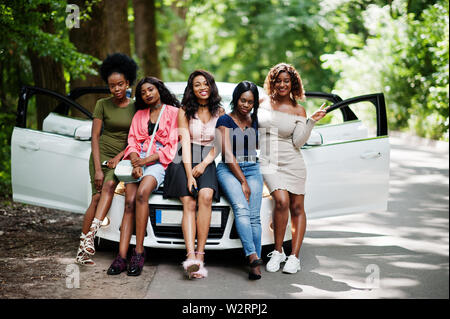 Groupe de cinq happy african american girls assis sur un capot de voiture. Banque D'Images