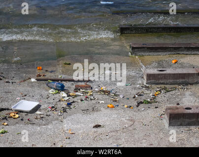 Les déchets dans le secteur de port sur le chemin de béton à l'eau. Bouteille en plastique, écorce d'orange et plusieurs autres pièces en plastique. Banque D'Images