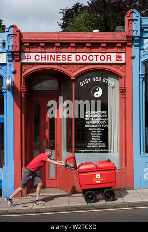 Un facteur poussant son chariot de courrier vers le passé, le médecin chinois sur le Morningside Road, Edinburgh, Scotland, UK. Banque D'Images