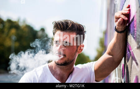 Beau homme fumant une e-cigarette, vapotant à l'extérieur Banque D'Images