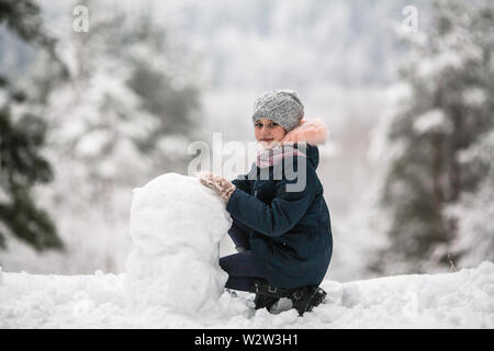 Fille mignonne avec bonhomme de neige en hiver. Banque D'Images