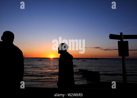 Silhouettes de deux personnes marchant le long de la mer comme revêtement le soleil se couche sur l'horizon à Colwell Bay sur l'île de Wight Banque D'Images