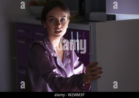 Peur femme prise dans l'acte de choix des aliments près de nuit au réfrigérateur). Banque D'Images