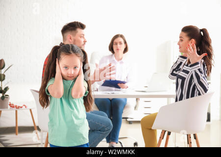 Enfant triste couvrant les oreilles avec les mains à cause de ses parents se disputer dans le bureau du psychologue Banque D'Images