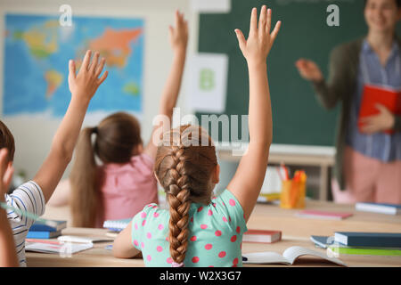 Cute little élèves sensibilisation mains pendant la leçon en classe Banque D'Images