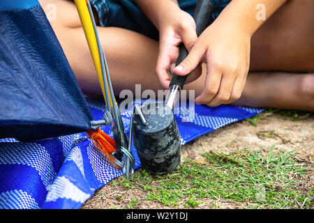 Main d'un enfant tenant un marteau en caoutchouc de fixation en acier martelé tente sur le sol. Banque D'Images