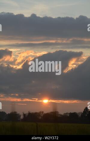 Séquence d'images d'un coucher du soleil avec le soleil apparaissant entre les bancs de nuages juste au-dessus de l'horizon. Banque D'Images