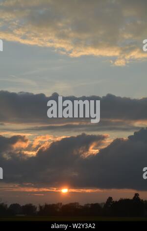 Séquence d'images d'un coucher du soleil avec le soleil apparaissant entre les bancs de nuages juste au-dessus de l'horizon. Banque D'Images