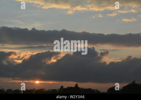 Séquence d'images d'un coucher du soleil avec le soleil apparaissant entre les bancs de nuages juste au-dessus de l'horizon. Banque D'Images