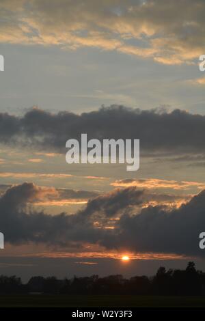 Séquence d'images d'un coucher du soleil avec le soleil apparaissant entre les bancs de nuages juste au-dessus de l'horizon. Banque D'Images