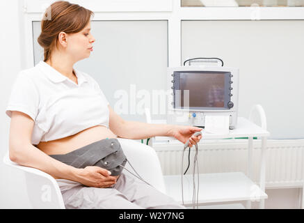 Pregnant woman sitting dans cardiotocography clinique effectuant (CTG). La courroie sur son ventre relié à l'Cardiotocograph alias machine Feta électronique Banque D'Images