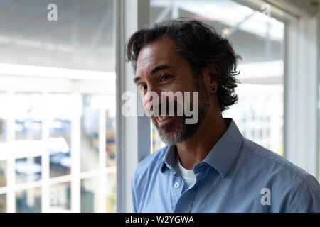 Happy businessman looking away while standing near window in office Banque D'Images