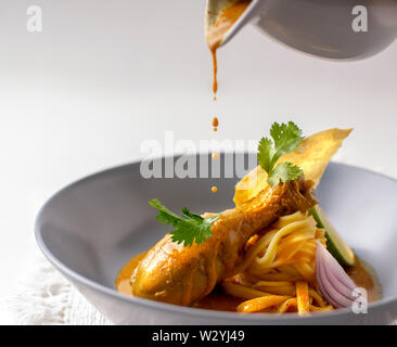 Jaune curry thaï pilons de poulet avec des nouilles aux œufs , lime, coriandre et nouilles aux oeufs frits croustillants dans un plat plaqué Banque D'Images