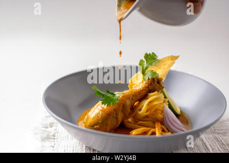 Jaune curry thaï pilons de poulet avec des nouilles aux œufs , lime, coriandre et nouilles aux oeufs frits croustillants dans un plat plaqué Banque D'Images