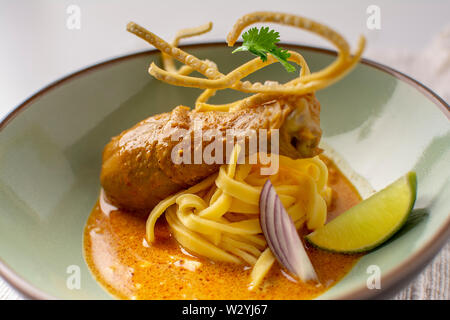 Jaune curry thaï pilons de poulet avec des nouilles aux œufs , lime, coriandre et nouilles aux oeufs frits croustillants dans un plat plaqué Banque D'Images