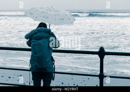 Woman with umbrella walking on beach sous la pluie . UK Banque D'Images