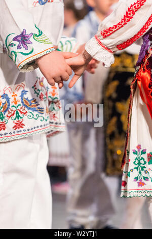 Près des mains de jeunes danseurs roumains effectuer une danse folklorique en costume folklorique traditionnel. Le folklore de Roumanie Banque D'Images