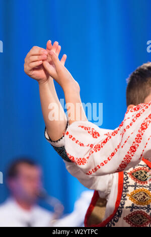 Près des mains de jeunes danseurs roumains effectuer une danse folklorique en costume folklorique traditionnel. Le folklore de Roumanie Banque D'Images