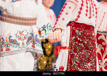 Près des mains de jeunes danseurs roumains effectuer une danse folklorique en costume folklorique traditionnel. Le folklore de Roumanie Banque D'Images