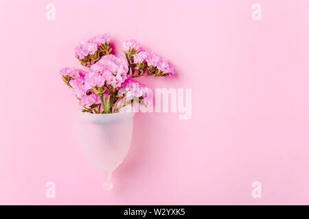 Coupe menstruelle blanche pour les femmes à côté de fleurs sur fond rose. Alternative écologique aux joints et les tampons. Concept Zéro déchet Banque D'Images