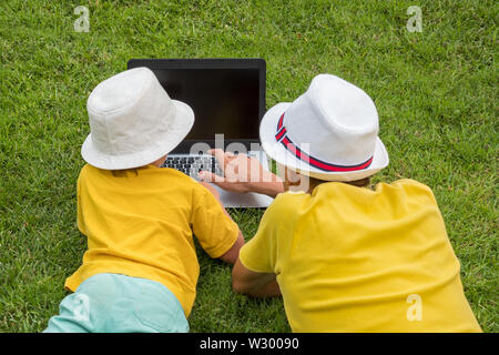 Avec Père Fils couché dans l'herbe près de l'ordinateur portable. Frères et sœurs et de gadgets à l'extérieur. Père et fils de passer du temps ensemble à l'extérieur. Homme avec garçon s'amusant sur Banque D'Images