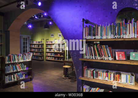 Forme d'onde spotlit pourpre partie de mur dans la bibliothèque pour enfants, avec des étagères. Bibliothèque Deichman Grunerlokka, Oslo, Norvège. Architecte : Aat Vos, 2019. Banque D'Images