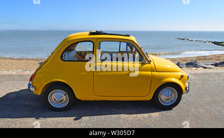 Fiat 500 jaune classique placée sur une promenade de bord de mer. Banque D'Images