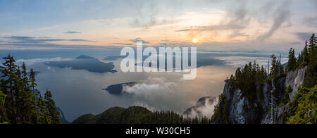 Vue panoramique de Female Hiker au sommet d'une montagne couverte de nuages pendant un été animé coucher du soleil. Pris sur le dessus de la Sommet, West Vancouver Banque D'Images
