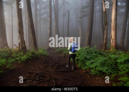 Fille d'aventure en randonnée sur un sentier dans les bois pendant un jour de pluie et de brouillard. Prises dans le Parc provincial Cypress, Vancouver, Colombie-Britannique, Canada. Banque D'Images