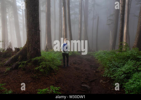 Fille d'aventure en randonnée sur un sentier dans les bois pendant un jour de pluie et de brouillard. Prises dans le Parc provincial Cypress, Vancouver, Colombie-Britannique, Canada. Banque D'Images