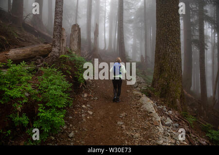 Fille d'aventure en randonnée sur un sentier dans les bois pendant un jour de pluie et de brouillard. Prises dans le Parc provincial Cypress, Vancouver, Colombie-Britannique, Canada. Banque D'Images