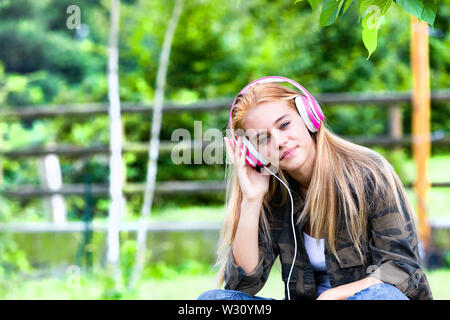 Jolie jeune femme blonde liste de la musique dans des écouteurs, campagne historique. Banque D'Images