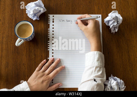 Je suis désolé écrits sur du papier avec du café sur la table en bois, les mains d'une personne close-up Banque D'Images