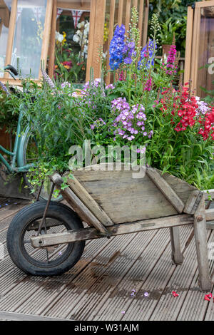 Vieille brouette et location en face d'une serre sur un affichage à l'RHS Hampton Court Flower Show 2019. Hampton Court, Surrey, Angleterre Banque D'Images